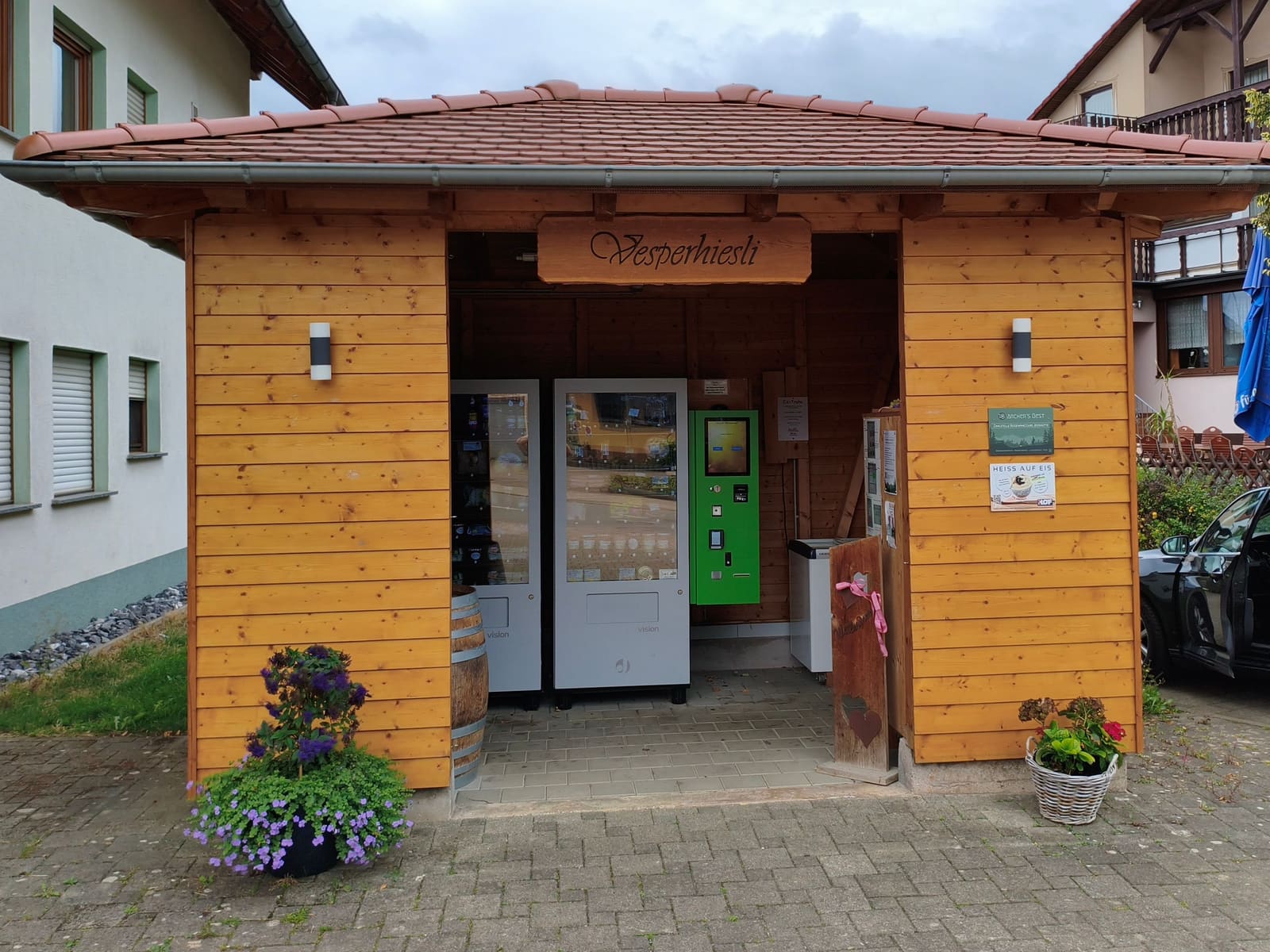 Das Vesperhiesli: Holzhütte mit Ziegeldach, darin die Automaten, davor Blumen