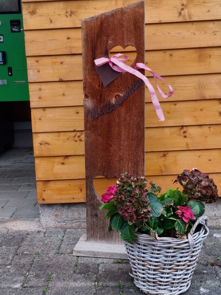 Altes Holzbrett mit Herzen und Schleife, davor ein Korb mit Hortensien