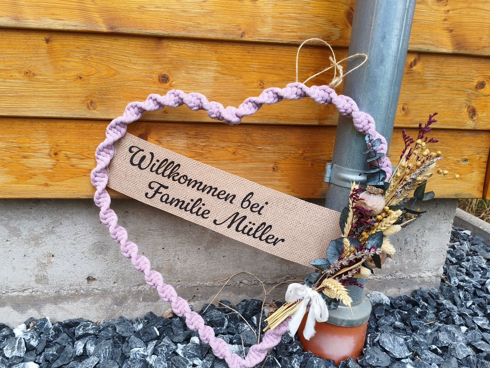 Geknüpftes lila Herz mit dem Schild „Willkommen bei Familie Müller“ an unserer Hütte