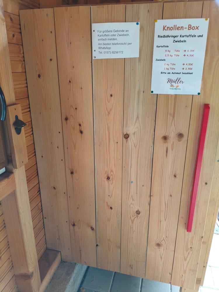 Holztür der Knollen-Box mit Preisaushang für Kartoffeln und Zwiebeln